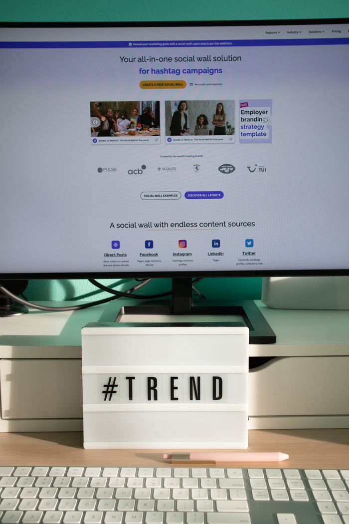 A sleek, contemporary desk arrangement featuring a lightbox that says #TREND and a computer display presenting a social wall solution.